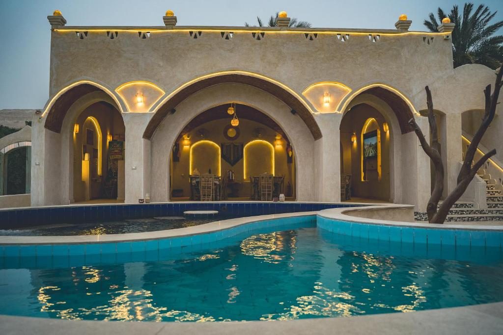 Arched lounge lit at dusk behind a curving blue pool