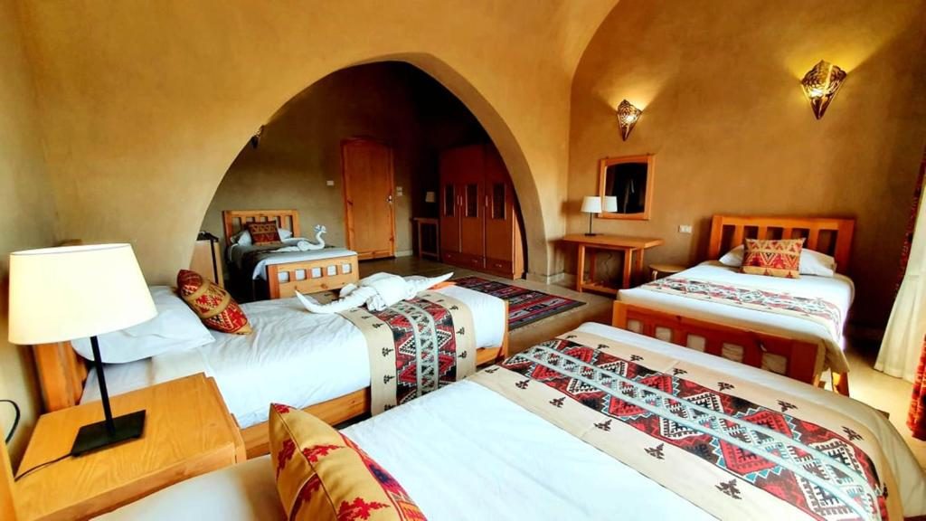 Mud-brick guest room with an arched alcove and three single beds with woven throws
