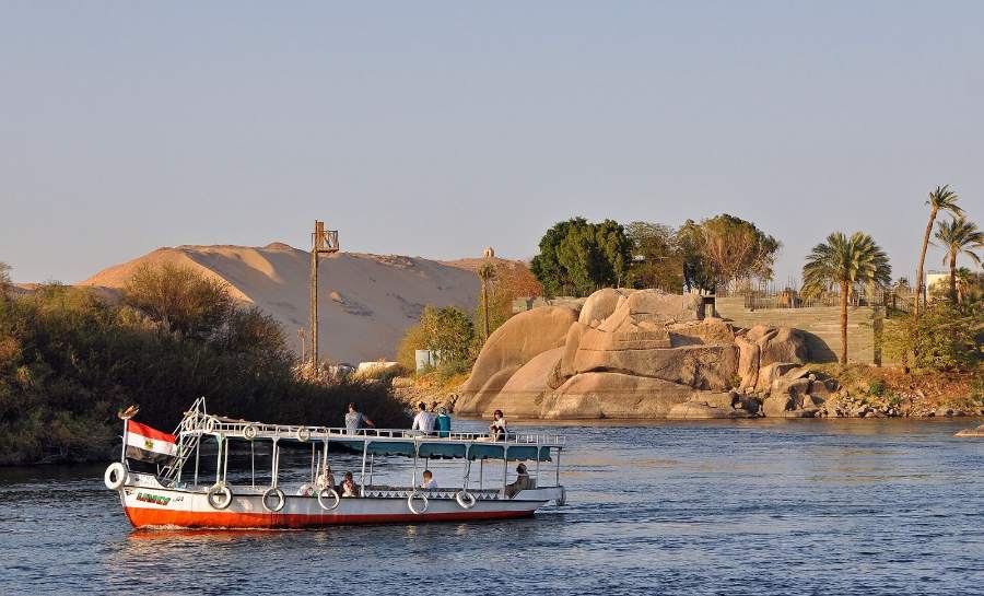 A Nile boat passing granite rocks and palms at Aswan